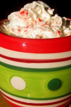 a red mug filled with whipped cream and candy canes on top of a wooden table