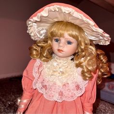 a doll with blonde hair wearing a pink dress and bonnet on top of her head