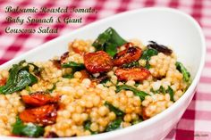 a close up of a bowl of food with spinach and tomatoes in it on a checkered table cloth