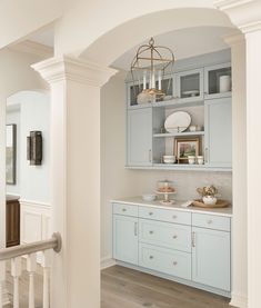 a white and blue kitchen with wooden floors, cabinets and chandelier hanging from the ceiling