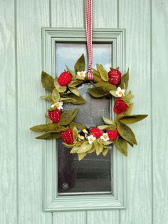 a green door with a wreath hanging from it's side and two strawberries on the front