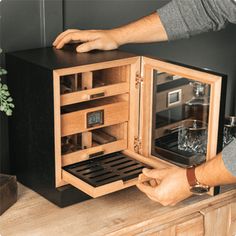 a man is opening the door to a small wooden cabinet that has wine glasses in it