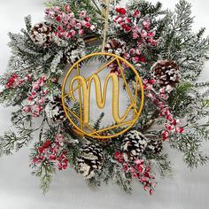 a christmas wreath with pine cones, berries and monogrammed letters hanging on the wall