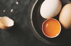 two eggs and an egg yolk in a bowl on a black tablecloth with other ingredients