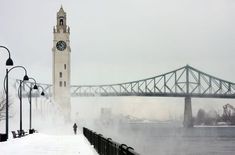 a tall clock tower towering over a city next to a bridge in the foggy day