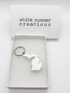 a white keychain with the shape of michigan on it in a gift box