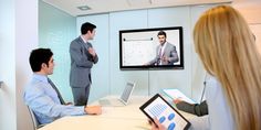 three people are sitting at a conference table and one person is on a video call