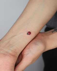 a ladybug tattoo on the left wrist is shown in black ink and has a red spot