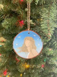 a christmas ornament hanging from a tree with lights in the background and an image of a woman's face on it