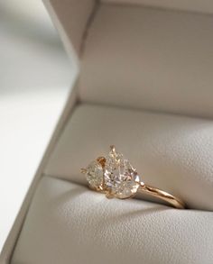 an engagement ring with three pear shaped diamonds in it's display box on a white surface