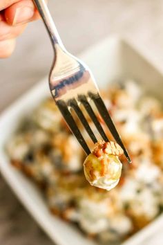 a fork with food on it is being held up by someone's hand over a casserole dish