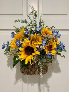 a basket filled with sunflowers and greenery hanging from a door handle in front of a white door