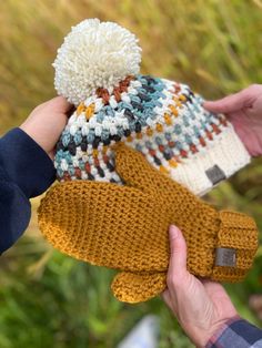 a person holding two knit mittens in their hands, one is yellow and the other is brown