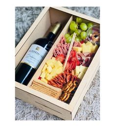 a wine bottle and several different types of food in a wooden box on the floor