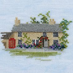 a cross stitch house with flowers on the front and side, in blue sky background