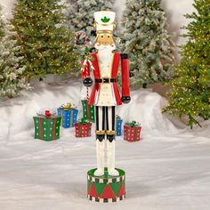 a nutcracker is standing in the snow with presents around him and trees behind it