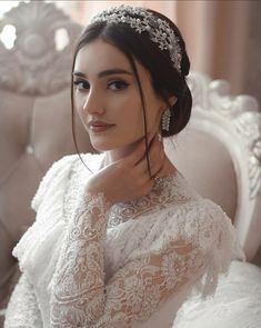 a woman in a white dress sitting on a couch wearing a tiara and jewelry