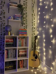 a room with bookshelves and string lights on the wall next to a guitar