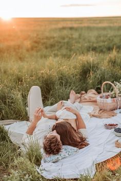 a woman laying on top of a white blanket next to a picnic table filled with food