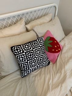 a white bed topped with two pillows and a pink strawberry pillow on top of it