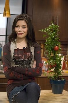 a young woman sitting on top of a wooden table next to a potted plant