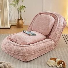 a dog laying on the floor next to a pink recliner chair with a book on it