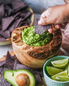 someone dipping guacamole into a wooden bowl surrounded by tortilla chips