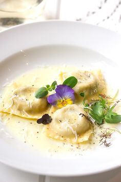 a white plate topped with ravioli covered in cheese and purple panacelli flowers