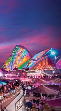 people are sitting at tables in front of an illuminated building with colorful lights on it