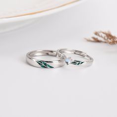 two white gold wedding rings with green leaves and a blue topazte, set on a plate