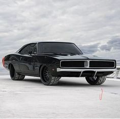 a black muscle car parked on top of a snow covered field next to the ocean