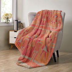 an orange and pink blanket sitting on top of a chair in front of a window