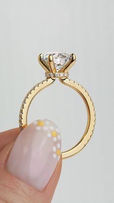 a hand holding a gold ring with a diamond on it's side and a white background