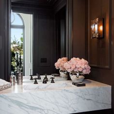 a bathroom sink with marble counter top next to a large mirror and vase filled with flowers