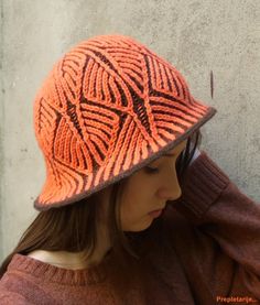 a woman wearing an orange knitted hat next to a concrete wall and looking at her cell phone