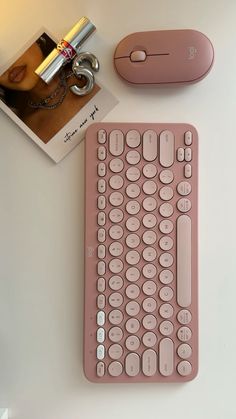 a pink computer keyboard sitting on top of a table next to a mouse and book