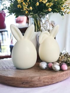 two white bunny shaped vases sitting on top of a wooden table next to flowers