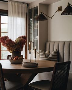 a wooden table topped with a bowl of fruit and a candle next to a window