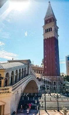 a tall clock tower towering over a city filled with buildings and people walking on the sidewalk