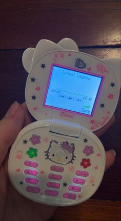 a hello kitty cell phone is being held up by someone's hand with the screen turned on