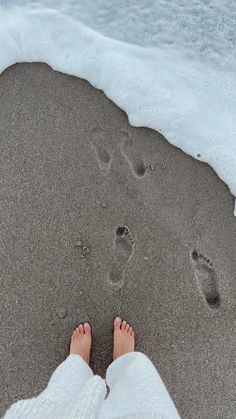 a person standing on top of a sandy beach next to the ocean with footprints in the sand