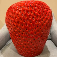 a large red strawberry sitting on top of a gray couch next to a white wall