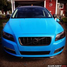 a blue car parked in front of a red house