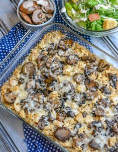 a casserole dish with mushrooms and cheese on it next to a bowl of salad