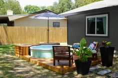 a small backyard with a hot tub and patio furniture in the foreground, next to a wooden deck