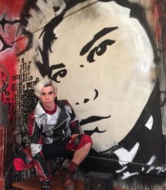 a man sitting on top of a wooden table in front of a wall with graffiti