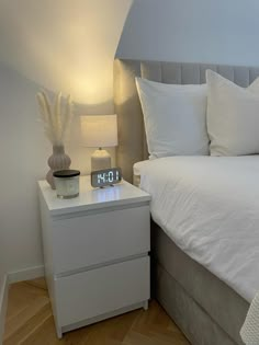 a white bed sitting next to a night stand with an alarm clock on top of it