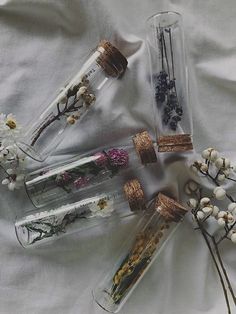 four glass bottles with dried flowers and branches in them sitting on a silver cloth covered surface