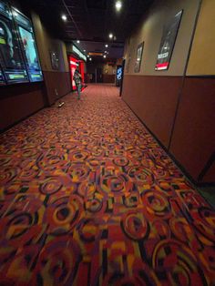 a carpeted hallway with red and yellow designs on the floor next to two televisions