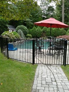 a patio with an umbrella over it next to a swimming pool and fenced in area